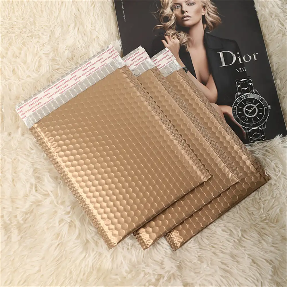 A trio of gold metallic bubble envelopes on a plush white fur background, accompanied by a Dior magazine advertisement, creating a luxurious and fashionable presentation.