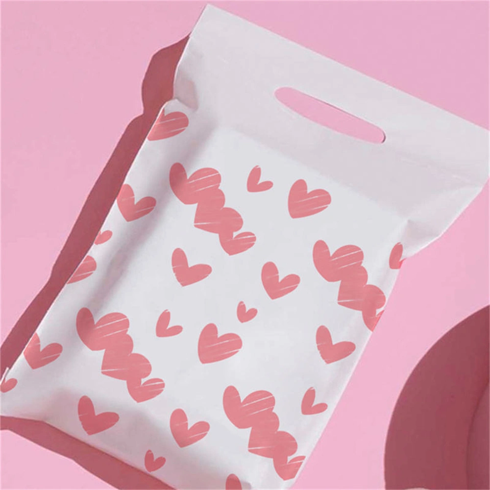 幾何学的な形がモダンな美しさを演出するピンクの背景に、赤いラブ・ハートがたくさんプリントされた持ち手付きの白い郵送用バッグ。
