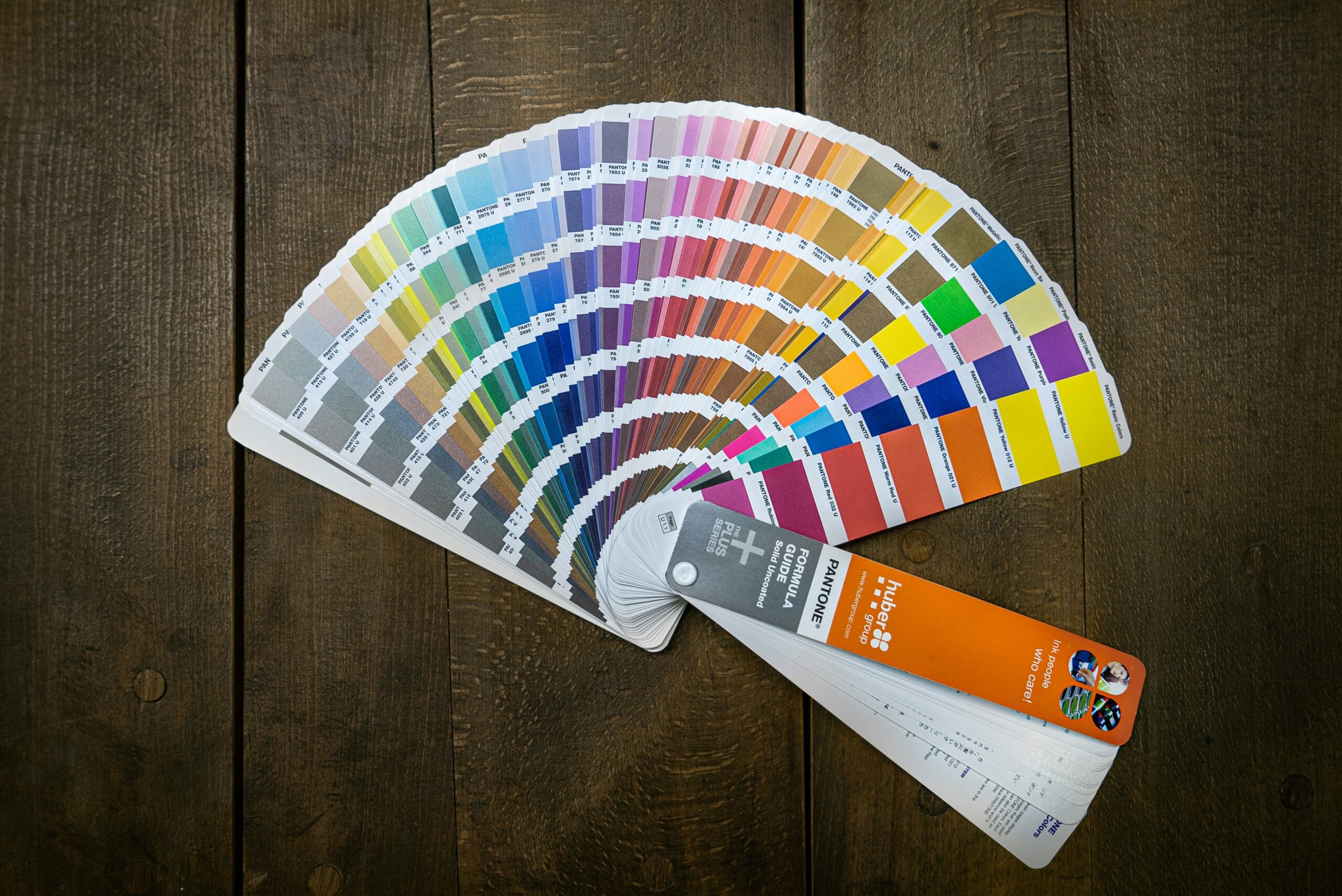 A Pantone color swatch fan is displayed open, revealing a spectrum of colors, arranged on a wooden surface.